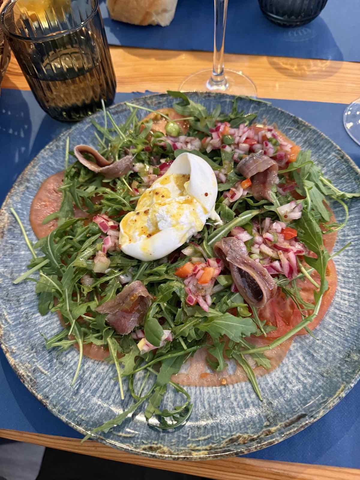 Carpaccio con rúcula, anchoas y huevo poché en plato cerámico de Bikainn